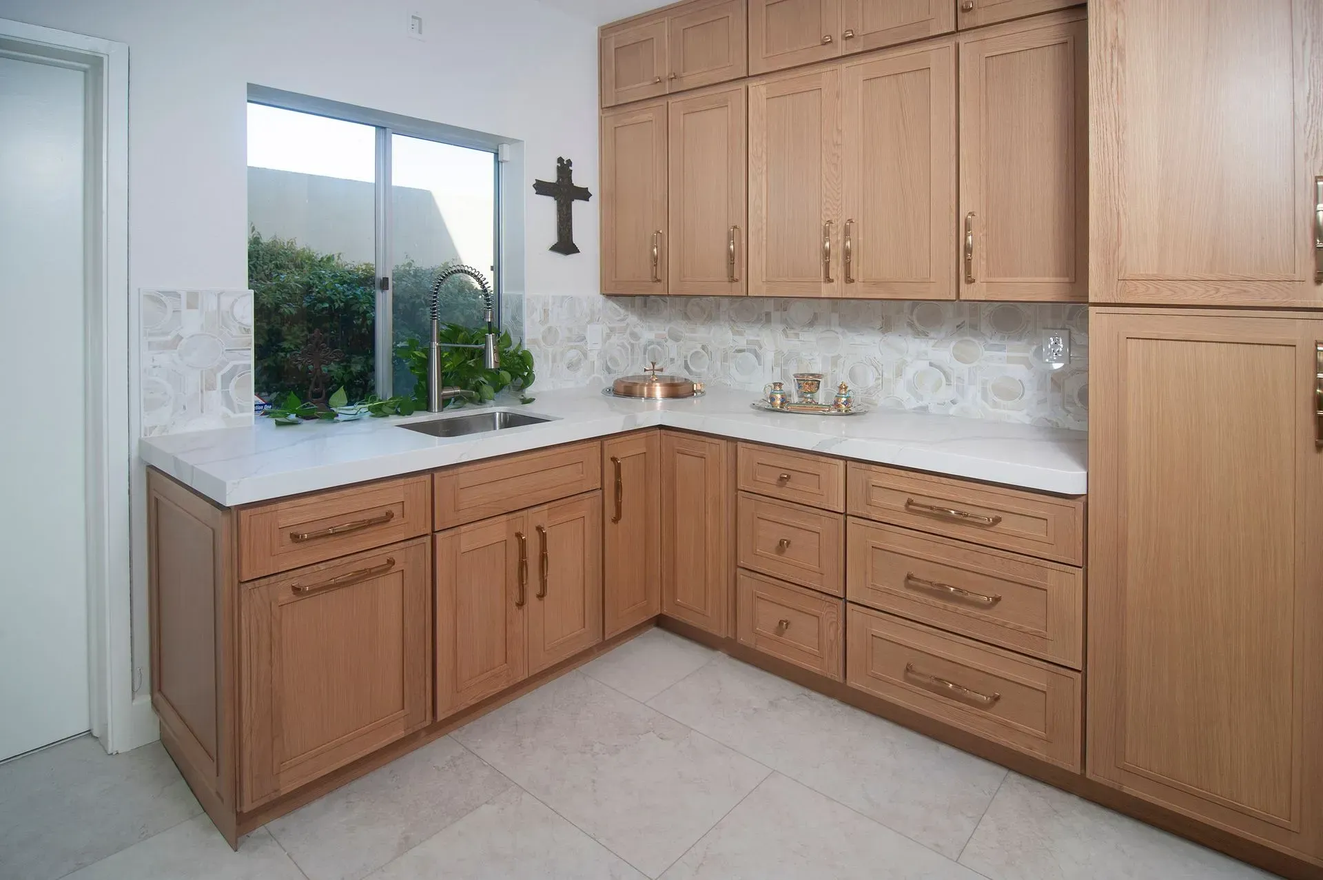 Bright modern kitchen with light wood cabinets, white countertops, and a window above the sink.