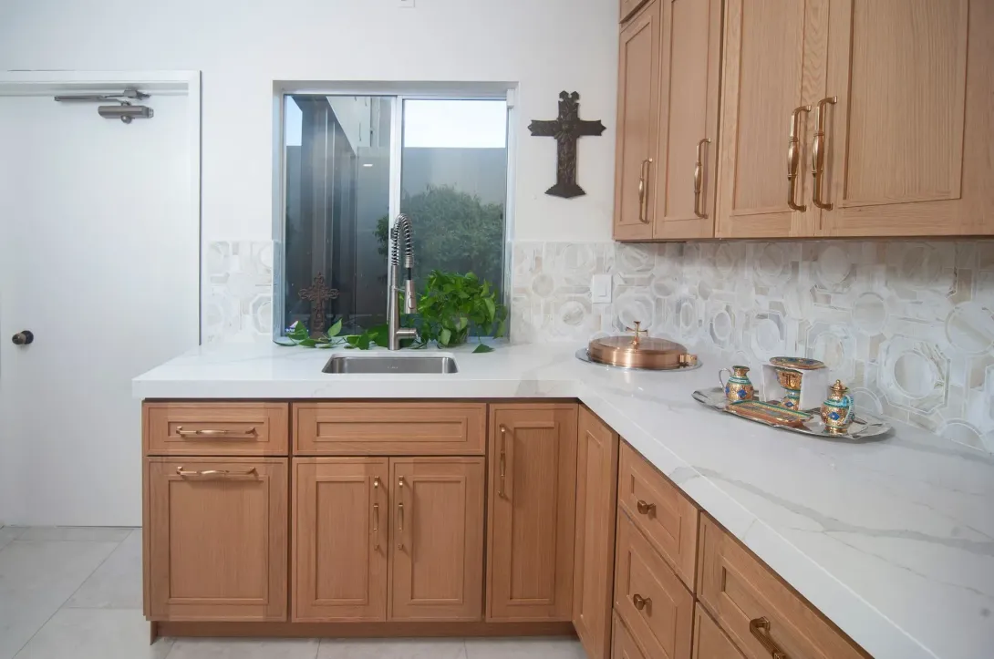 Bright kitchen with wood cabinets, white countertops, a window over the sink, and a wall cross.
