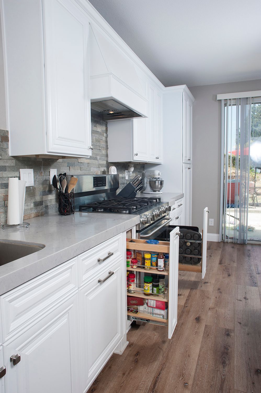 White kitchen with pull-out spice rack, gray countertops, and hardwood floors.
