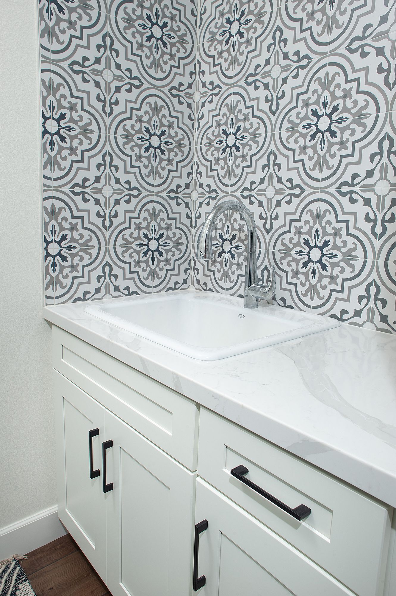 Laundry room with white cabinets, patterned tile backsplash, and chrome faucet.