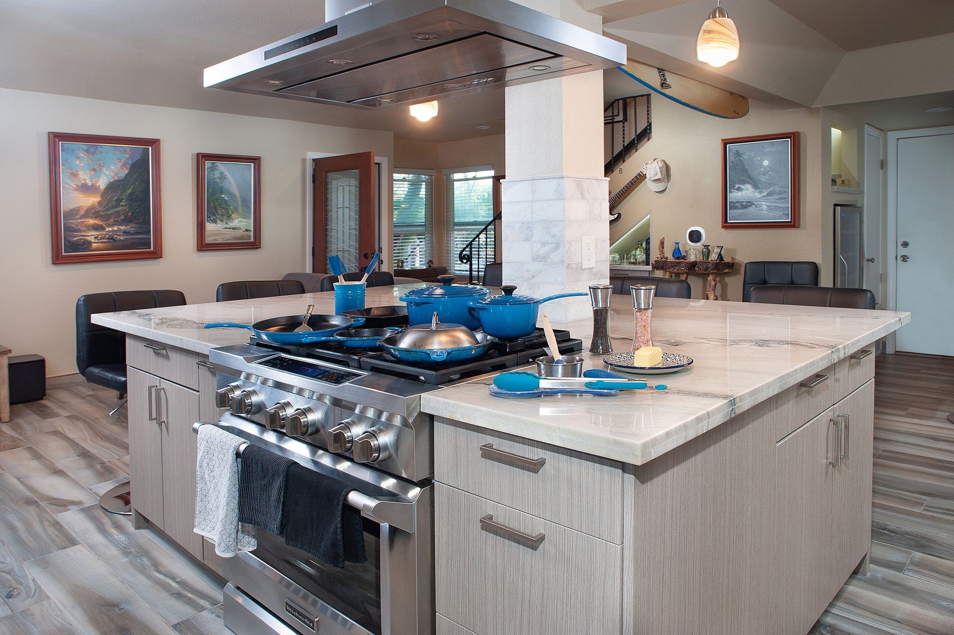 Modern kitchen with large island, stainless steel appliances, blue cookware, and artwork.