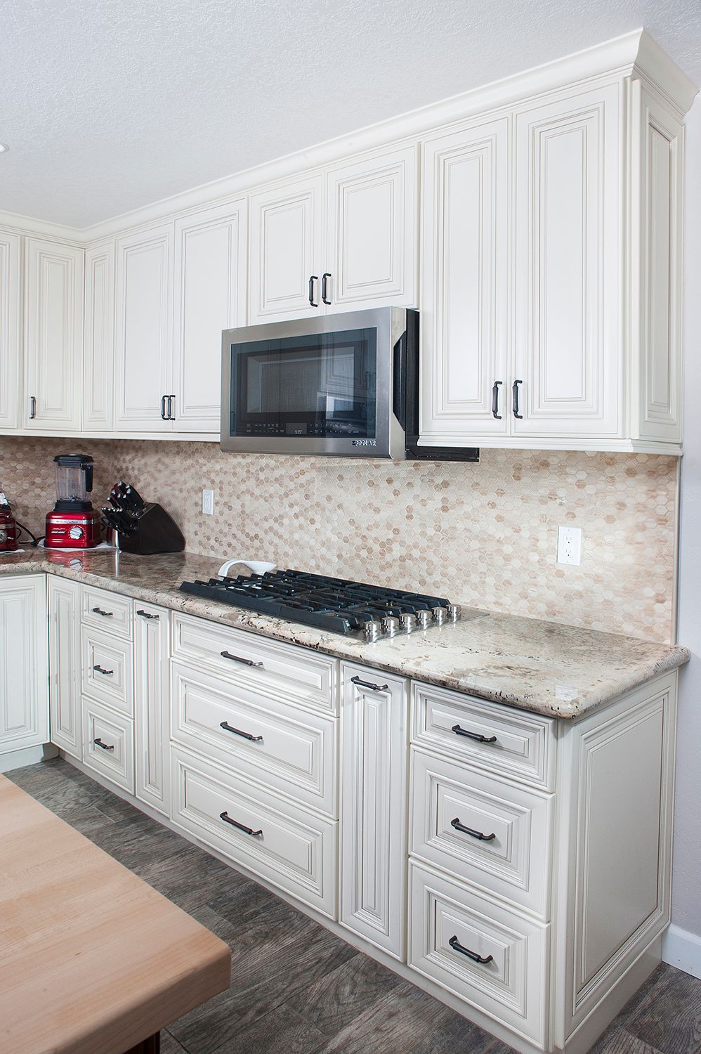 Cream-colored kitchen with cabinets, a gas stove, and a microwave. The backsplash is mosaic tile.