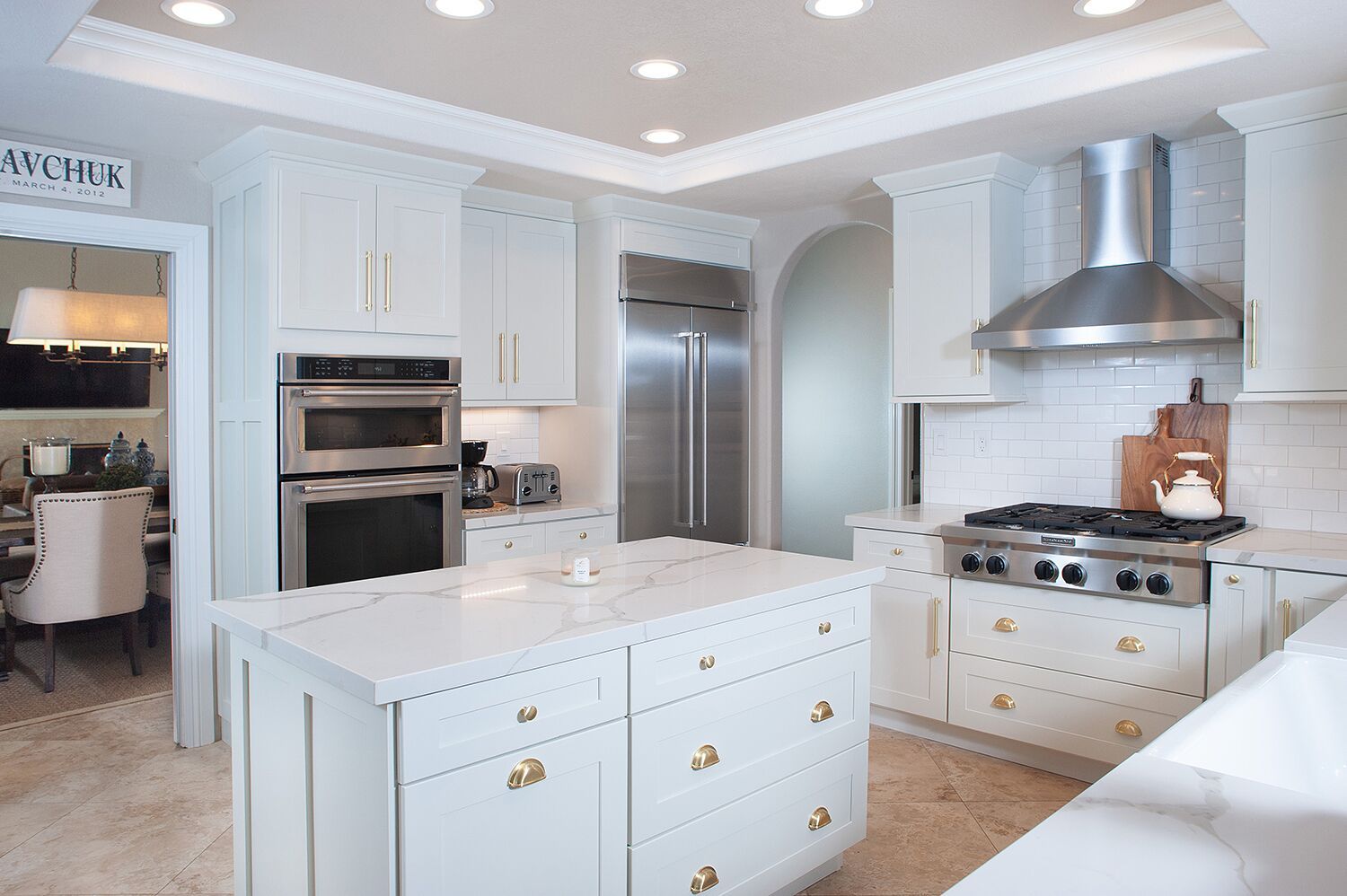 White kitchen with island, stainless steel appliances, and white cabinets; a luxury kitchen.