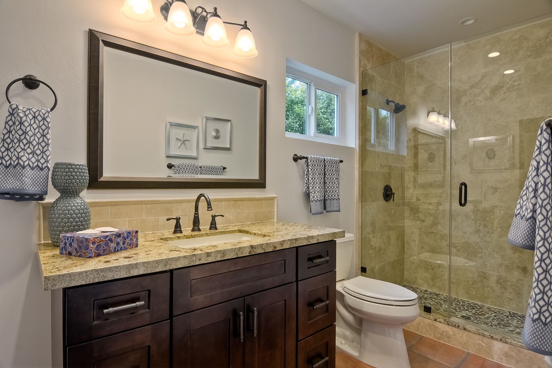 Bathroom with dark wood vanity, large mirror, glass shower, beige tile, and a window.
