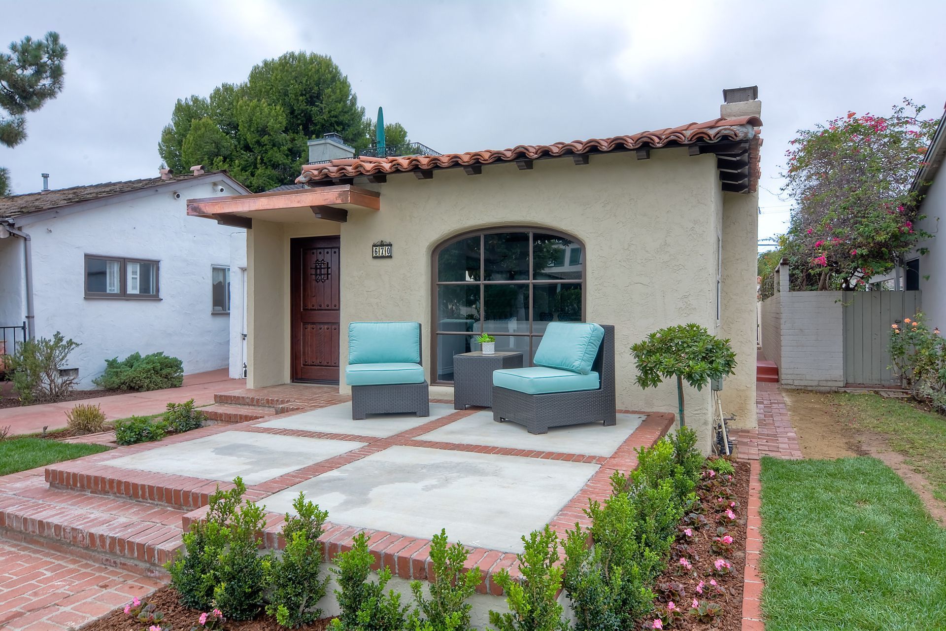 Charming stucco house with terracotta roof, small patio with teal chairs, and green lawn.