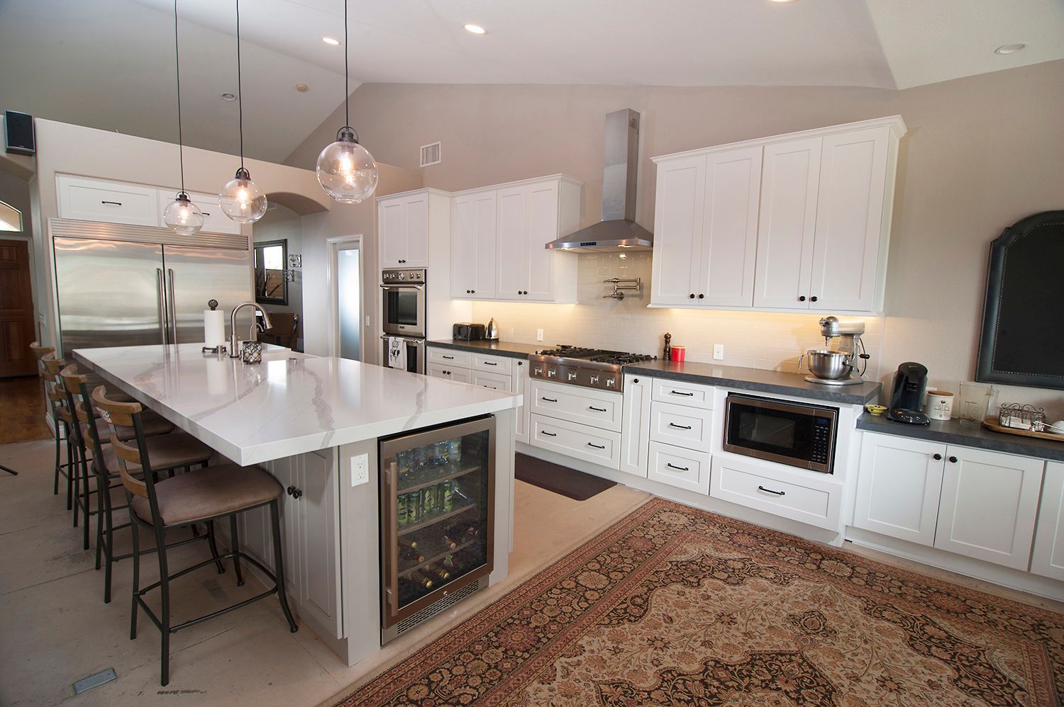 Modern white kitchen with island seating and appliances, including a wine fridge.