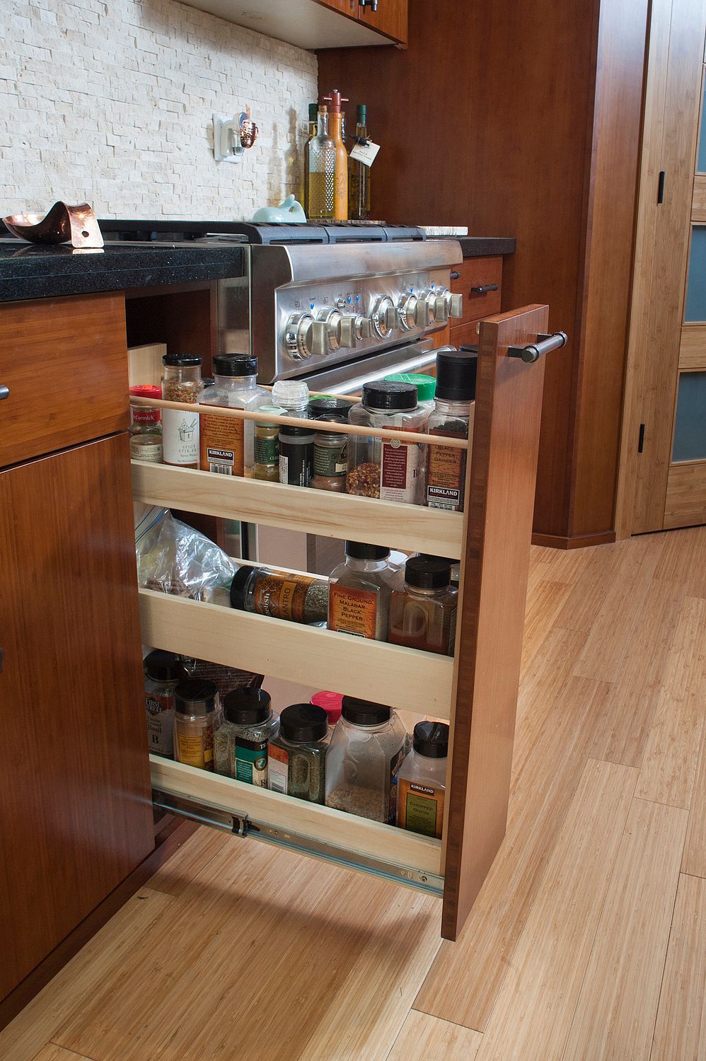 Wooden kitchen spice rack, partially pulled out, filled with various spice containers.
