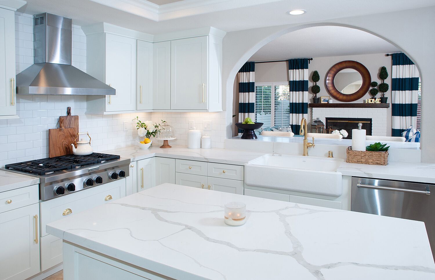 White kitchen with marble countertops, stainless steel appliances, and archway to living room.