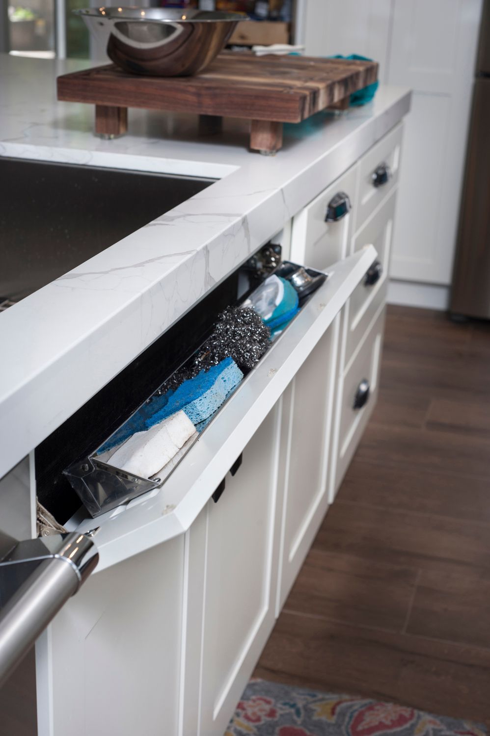 A kitchen island with a built-in pull-out storage drawer containing a water bottle. White cabinetry with marble countertop.