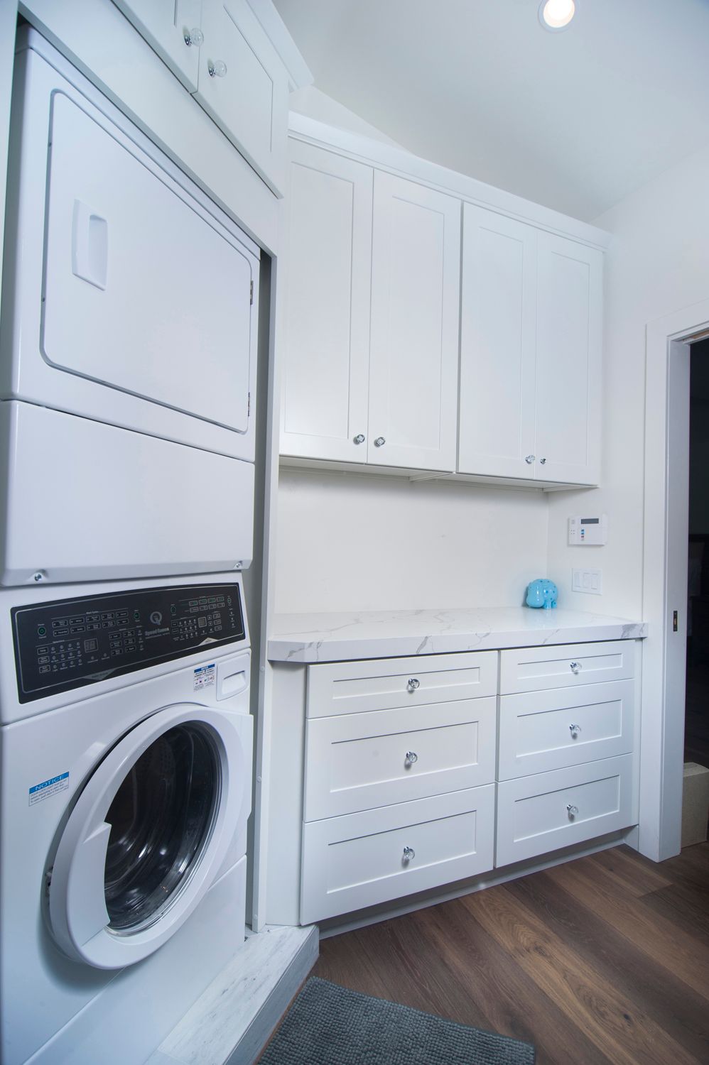A small, bright laundry room with a stacked washer and dryer, white cabinets, and a countertop.