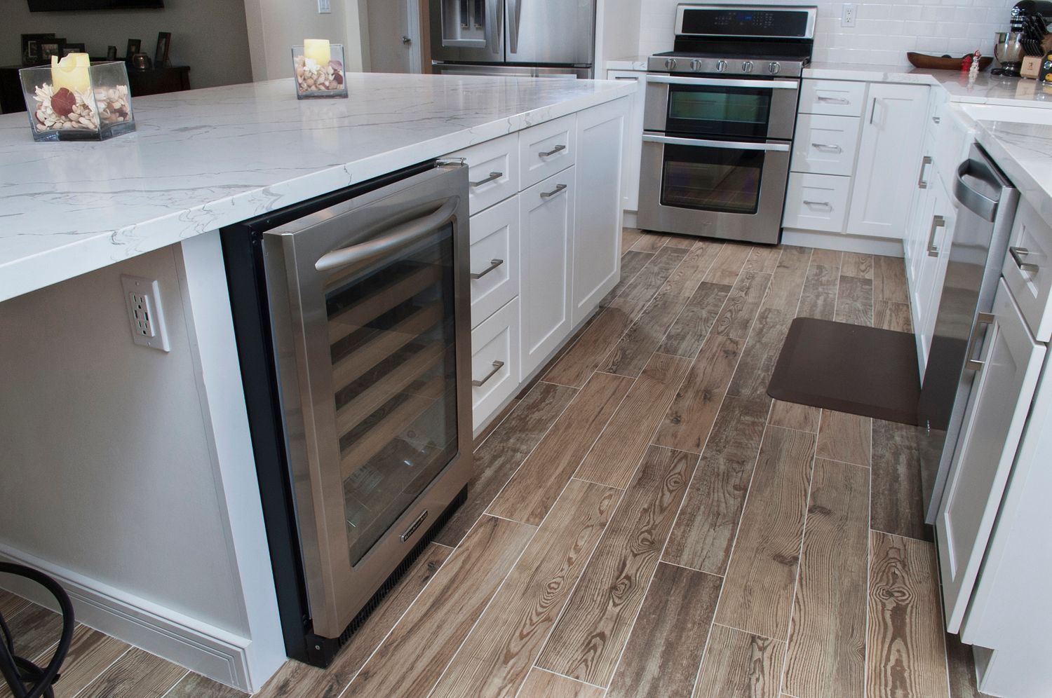 Kitchen with white cabinets, island, wine cooler, stainless steel appliances, wood-look tile floor.