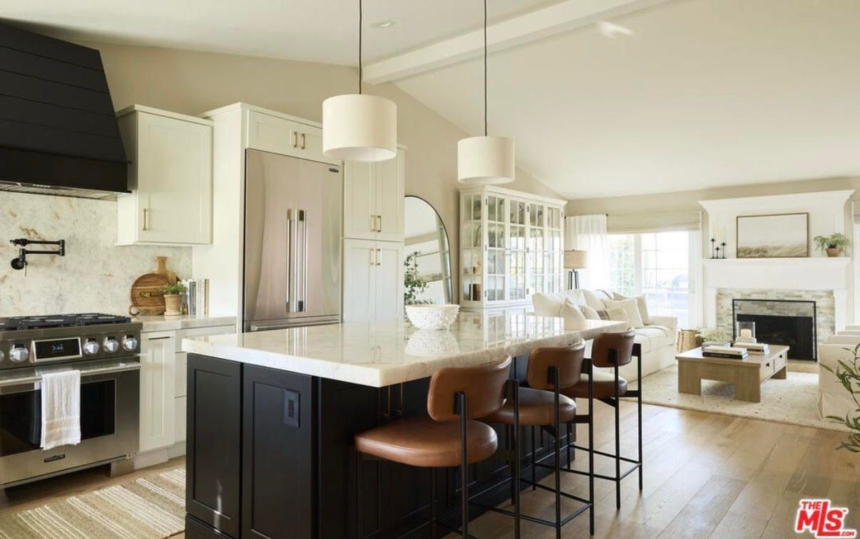 Open-concept kitchen with island, seating, and connected living room, featuring white and dark cabinetry.