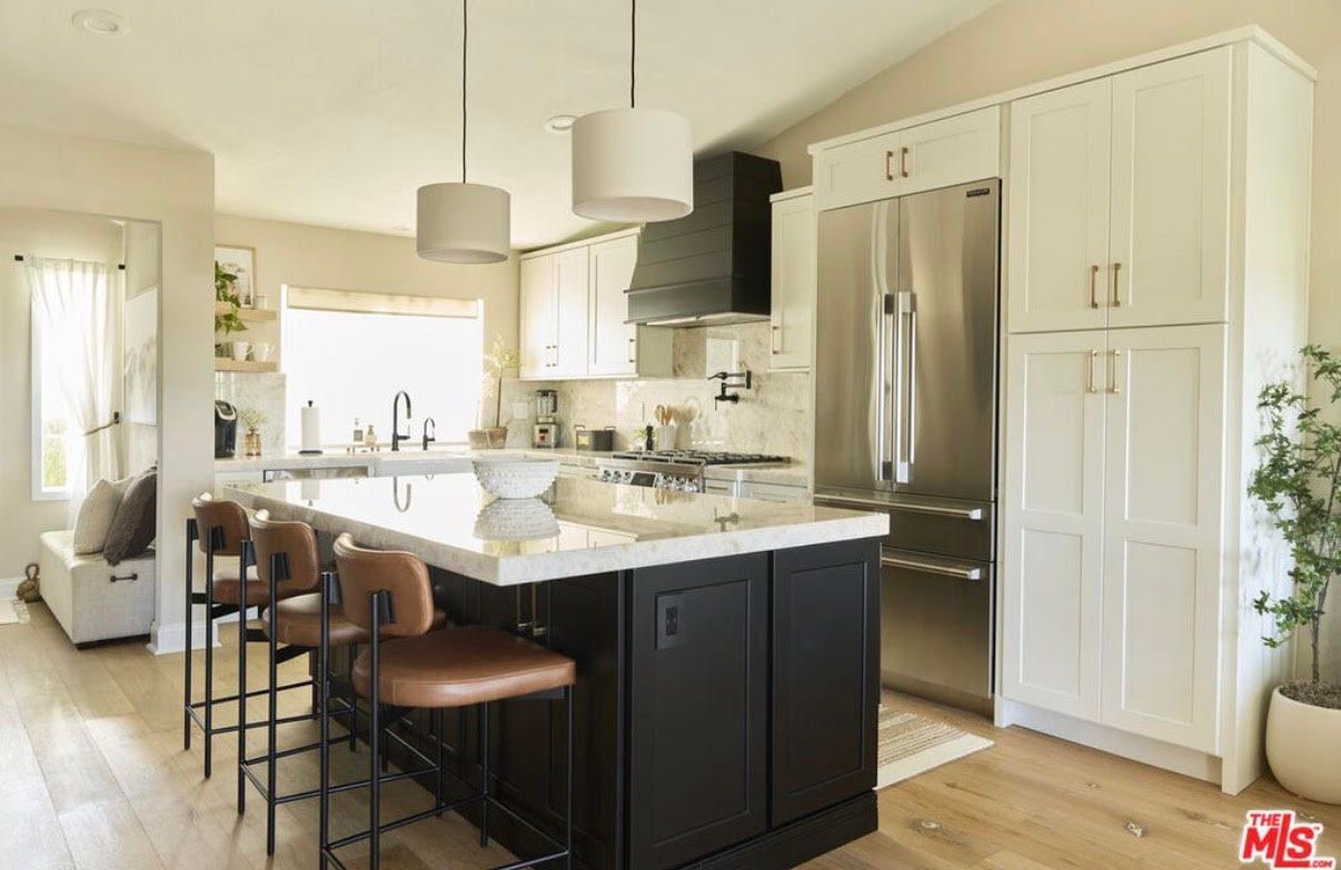 Modern kitchen with island, stainless steel refrigerator, white cabinets, and black range hood.