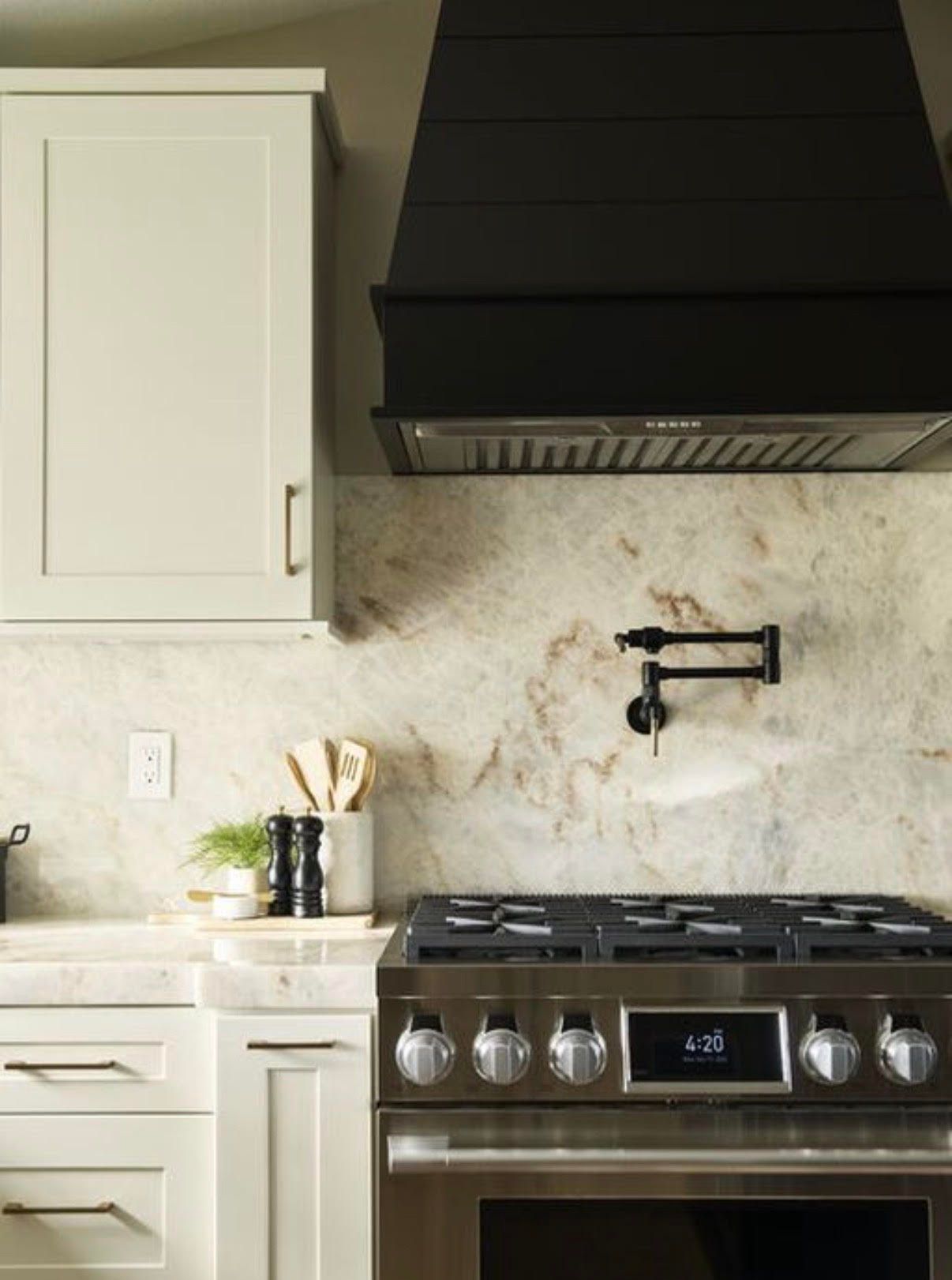 Kitchen with stainless steel range, black hood, light cabinets, and marble backsplash.