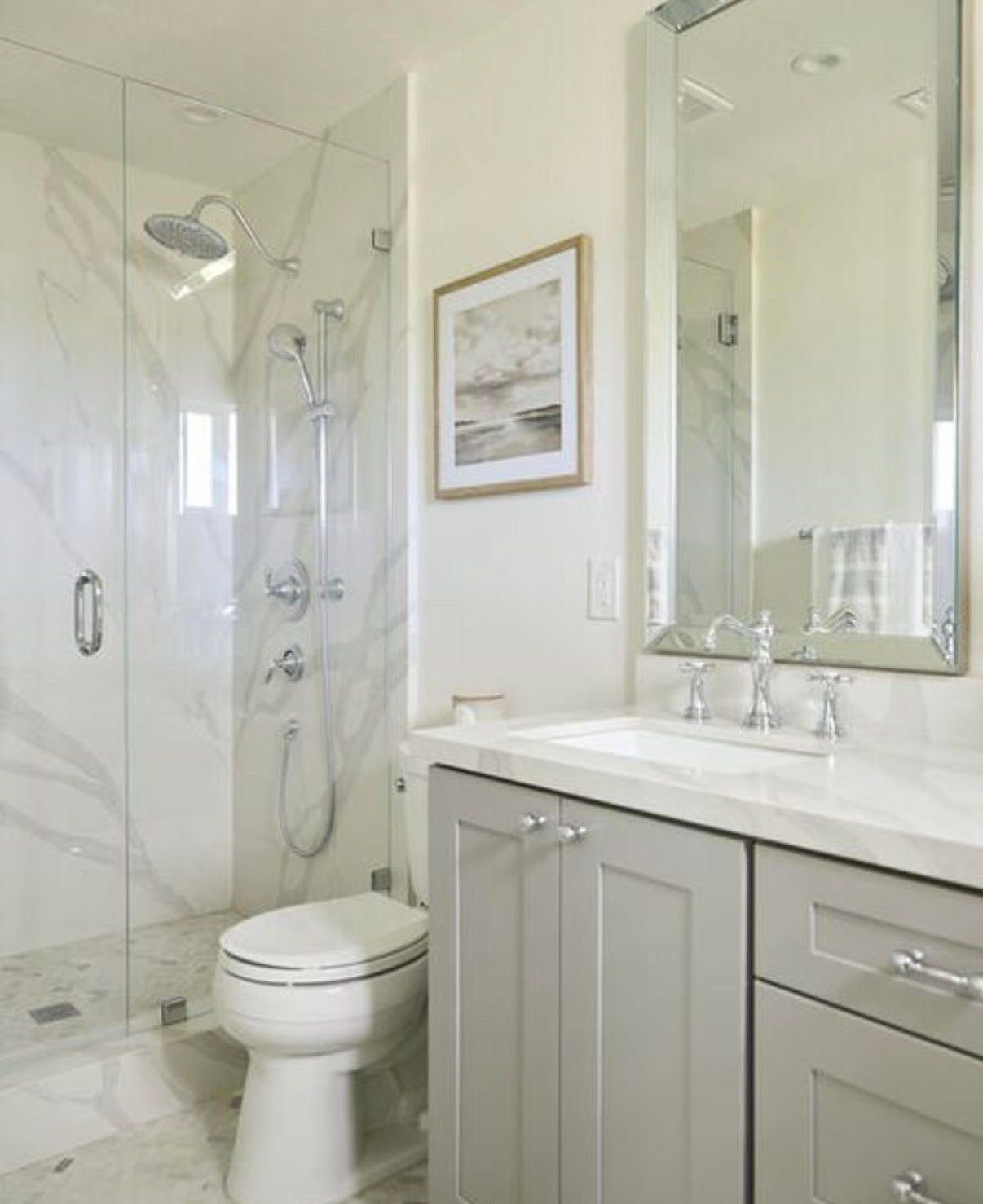 Bathroom with marble tile, glass shower, gray vanity, and framed artwork.