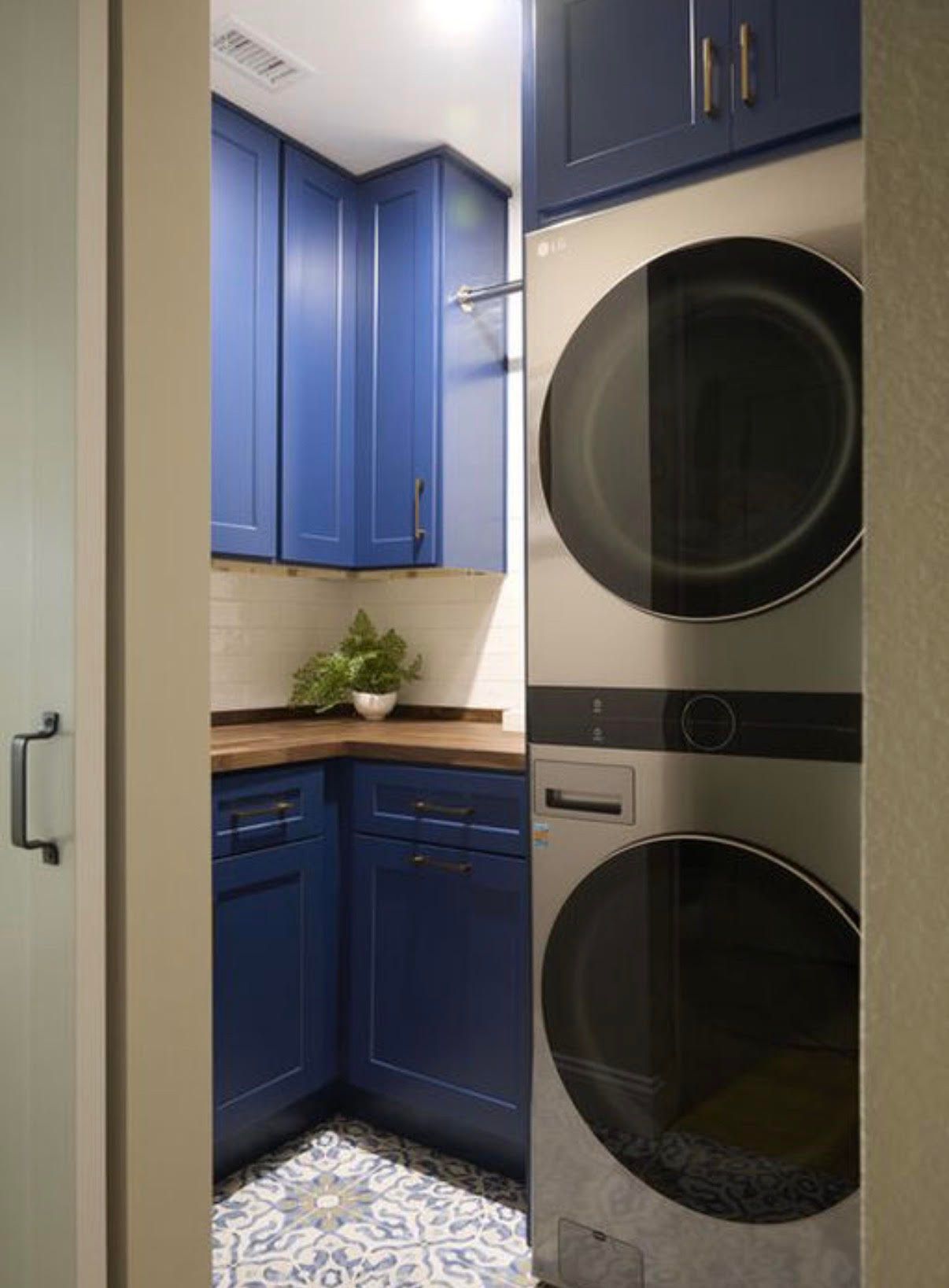 Blue laundry room with stacked washer and dryer, cabinets, and patterned floor.