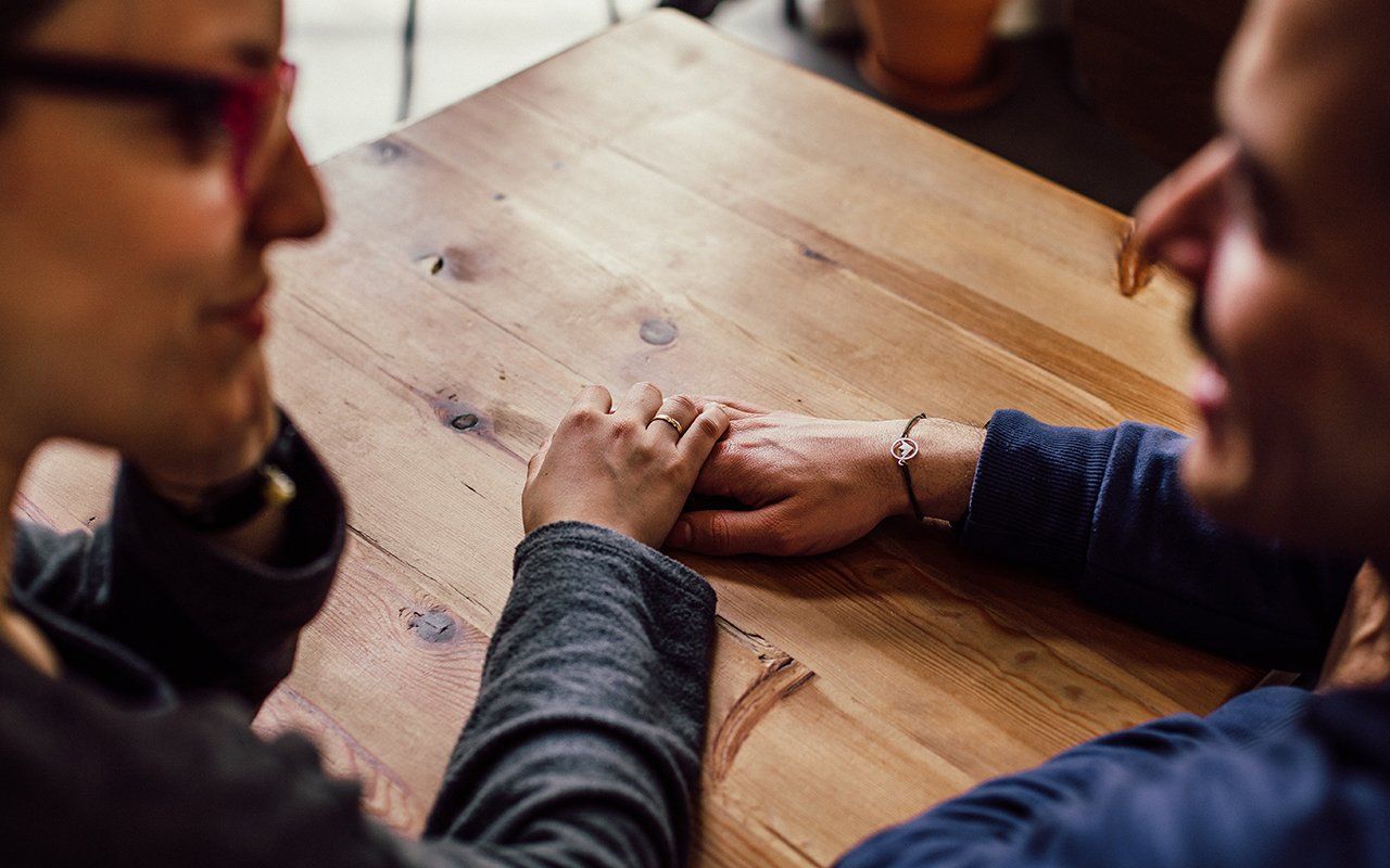 A man and a woman are sitting at a table holding hands.