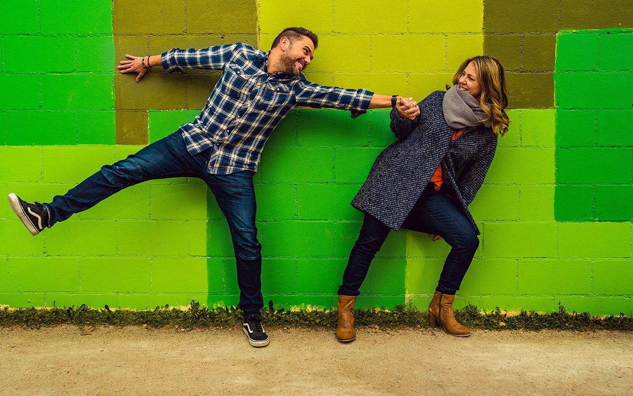 A man and a woman are standing next to each other in front of a green wall.