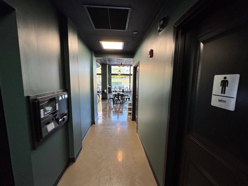 Narrow hallway with dark doors, restroom sign, and a bright seating area at the end.