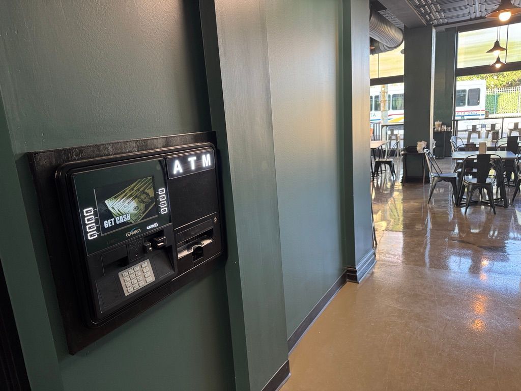 Wall-mounted ATM kiosk in a hallway beside a restaurant dining area