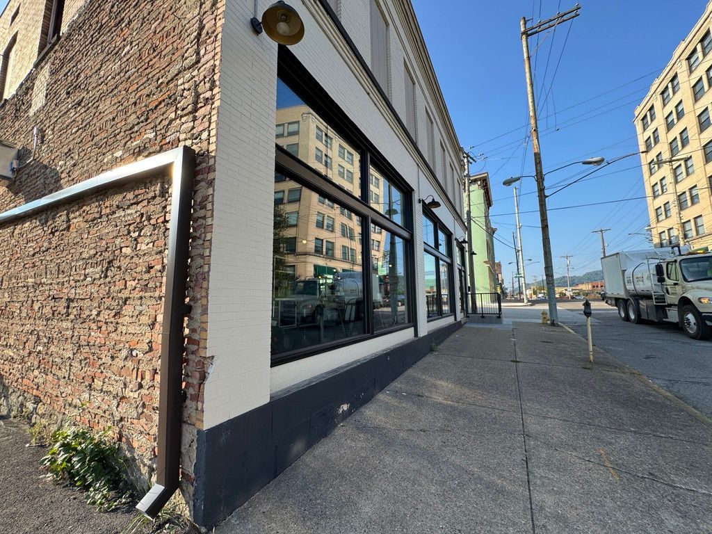Street corner with a brick building, large windows, sidewalk, parked truck, and overhead utility poles under clear sky