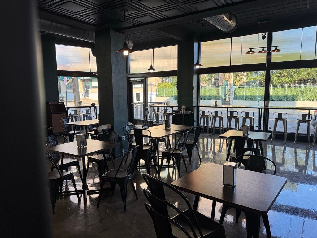Empty modern café with black tables and chairs, large windows, and sunlight reflecting on the floor.