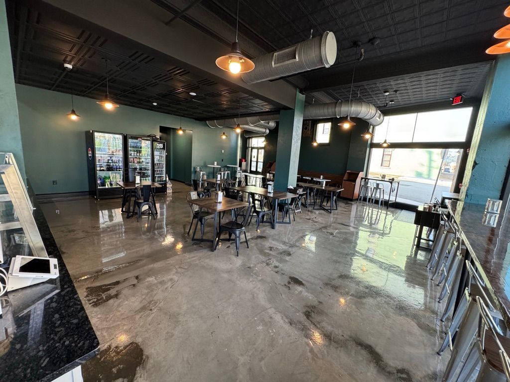 Empty modern cafe with tables and chairs, wet reflective floor, dark ceiling, and large windows.