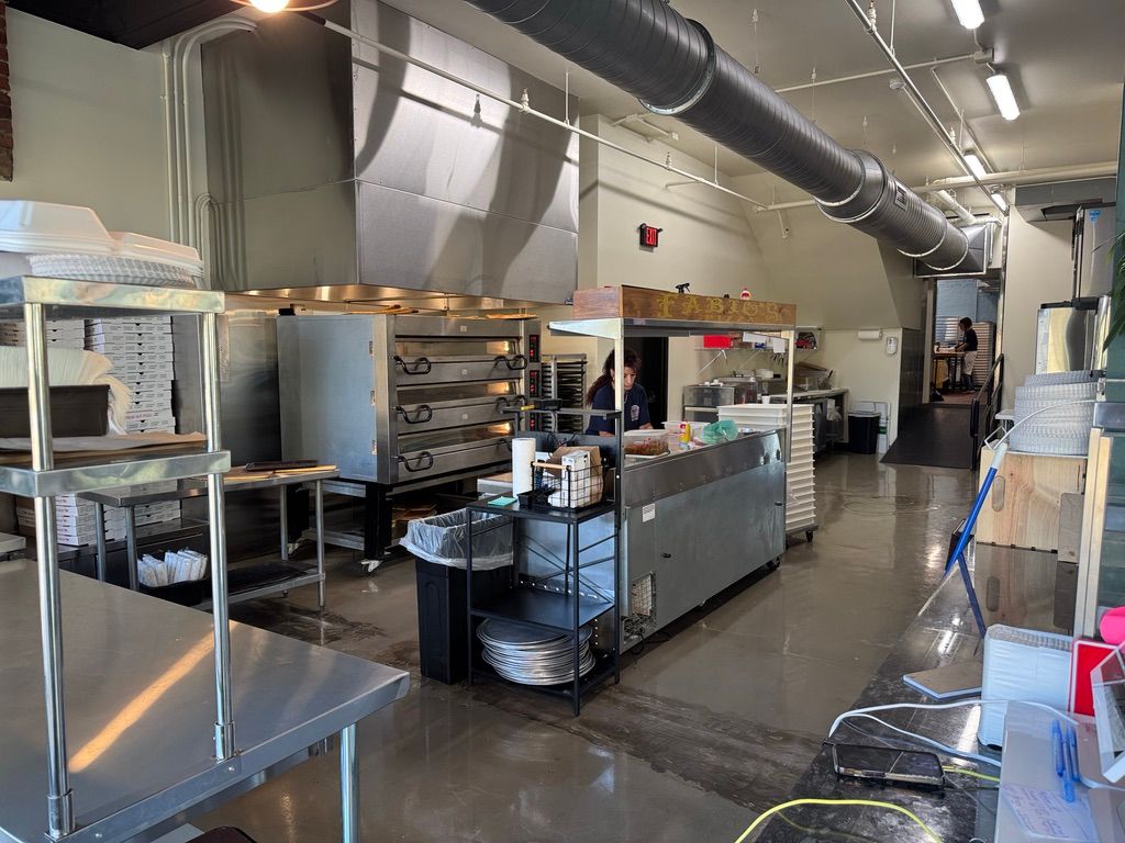 Commercial kitchen with stainless steel equipment, prep counters, and large ventilation hoods.