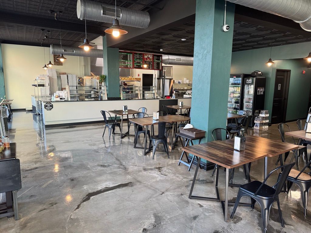 Empty modern café with scattered tables and chairs, teal columns, and a counter in the background