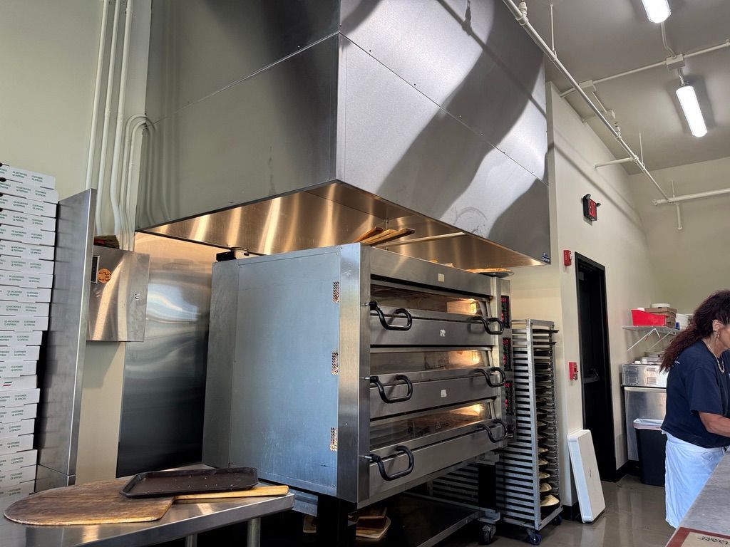 Commercial kitchen with stainless steel oven and large ventilation hood, with a person standing nearby