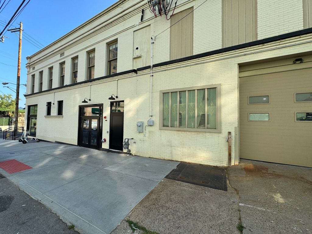 Street view of a beige commercial building with sidewalk, windows, and a black storefront entrance