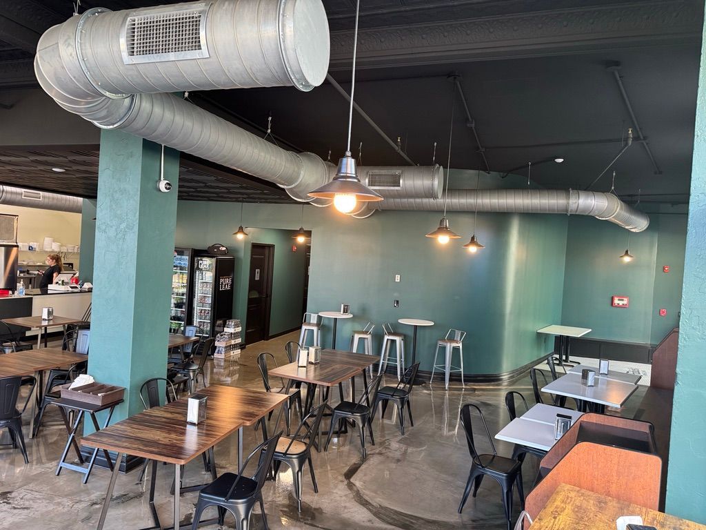 Empty modern restaurant with teal walls, exposed ductwork, and scattered tables and chairs