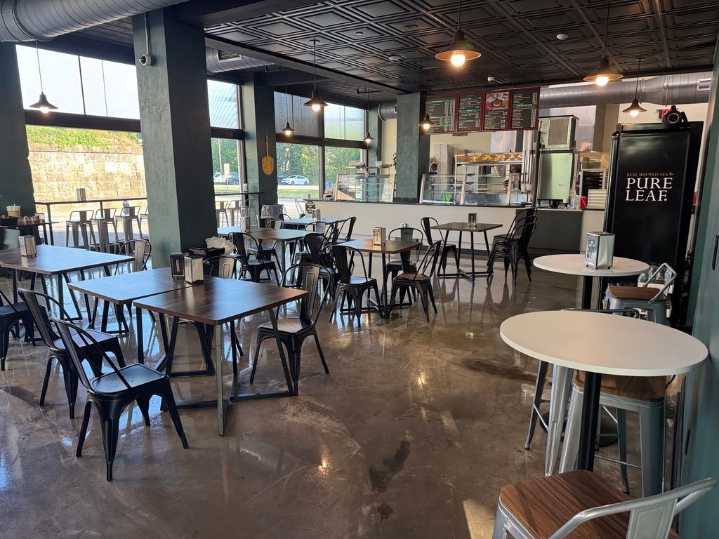 Empty café interior with wooden tables, black chairs, and a counter under decorative ceiling panels.