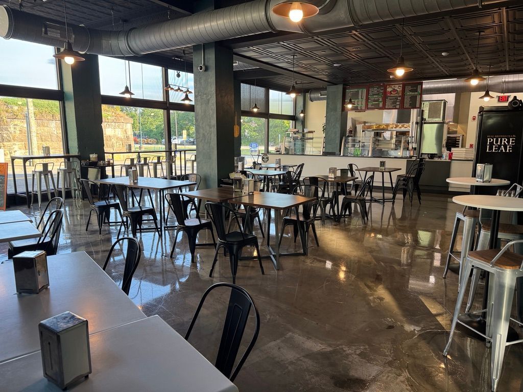 Empty cafe interior with tables and chairs, polished floor, and warm hanging lights near large windows
