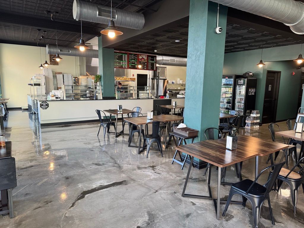 Empty cafe seating area with metal tables and chairs, polished concrete floor, and a counter in back