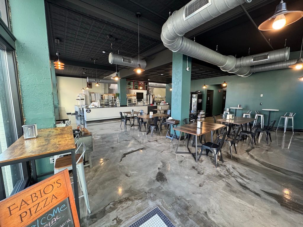 Industrial-style café with turquoise columns, exposed ducts, and scattered tables and chairs under warm lights