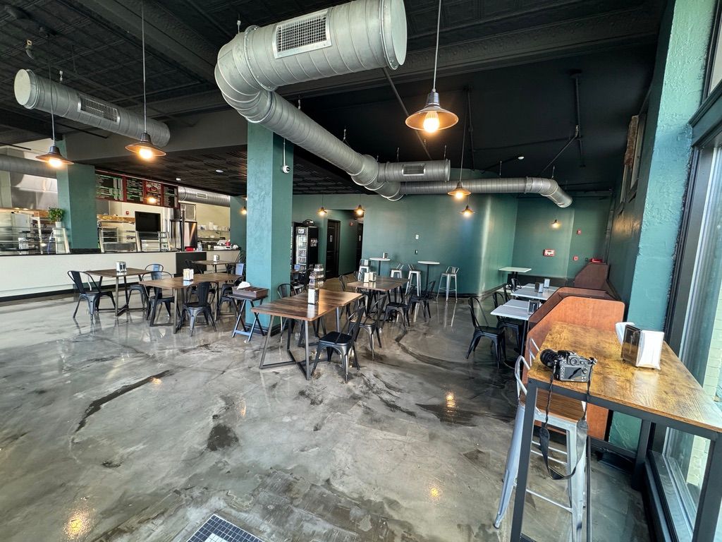Modern café interior with tables, chairs, teal columns, exposed ductwork, and concrete floors