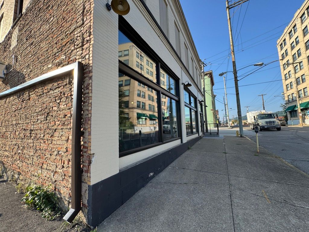 Urban sidewalk beside a brick building with storefront windows on a sunny street