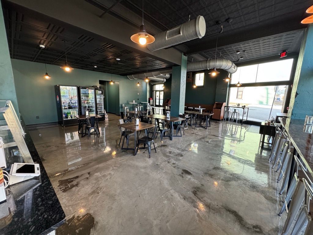 Empty modern café with tables, chairs, glossy concrete floor, and large windows letting in daylight