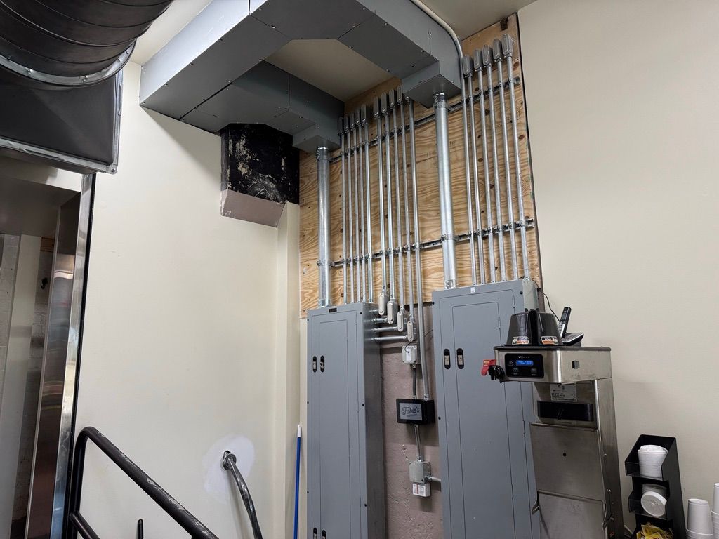 Electrical service panels with exposed conduit and gray metal boxes in a utility room