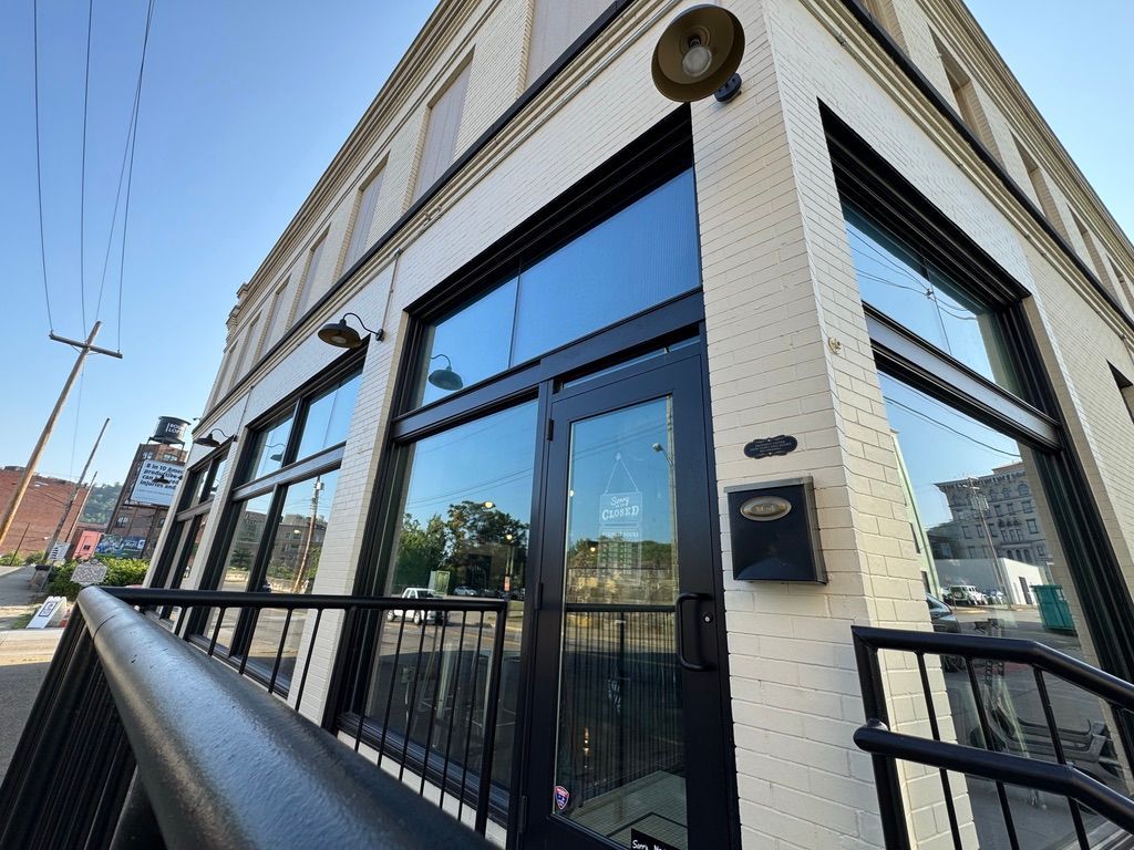 Corner storefront with glass windows, black railings, and a white brick facade on a sunny street