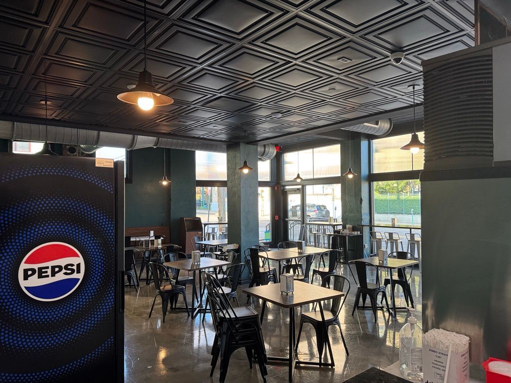 Empty modern café with Pepsi-branded counter, black tables, patterned ceiling, and large windows.