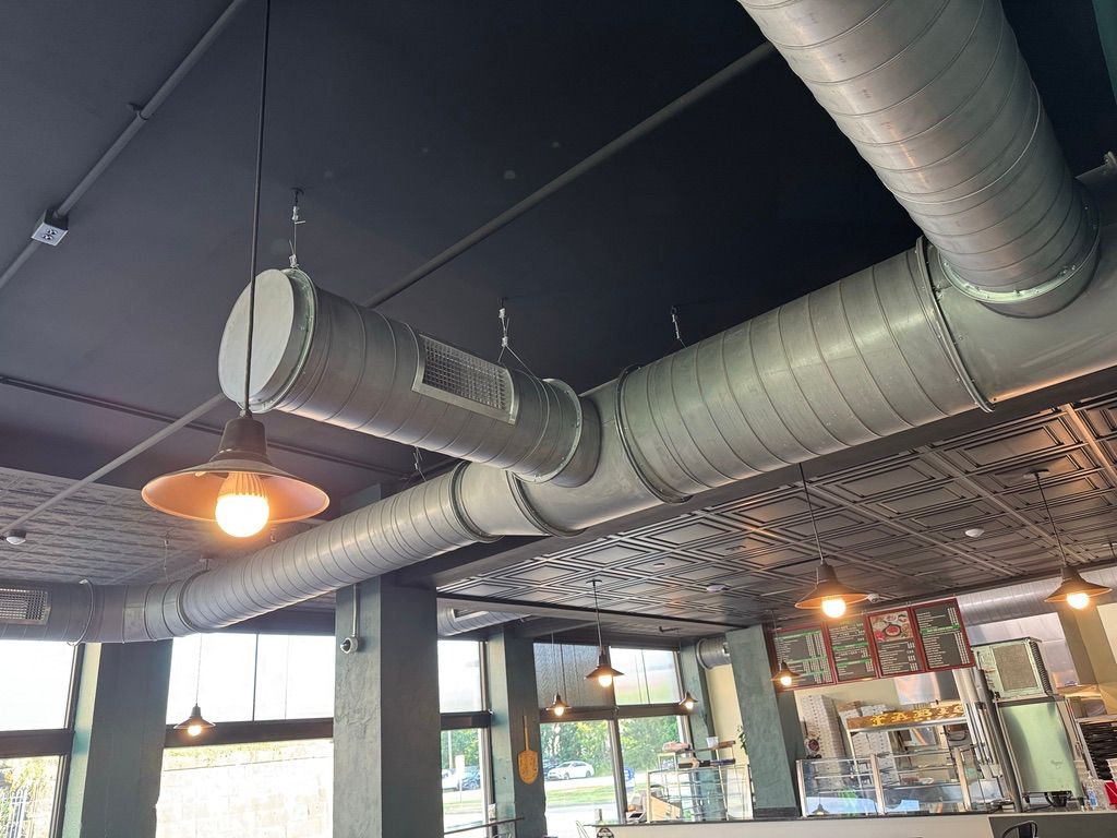 Industrial-style café interior with exposed silver ducts, warm hanging lights, and large windows