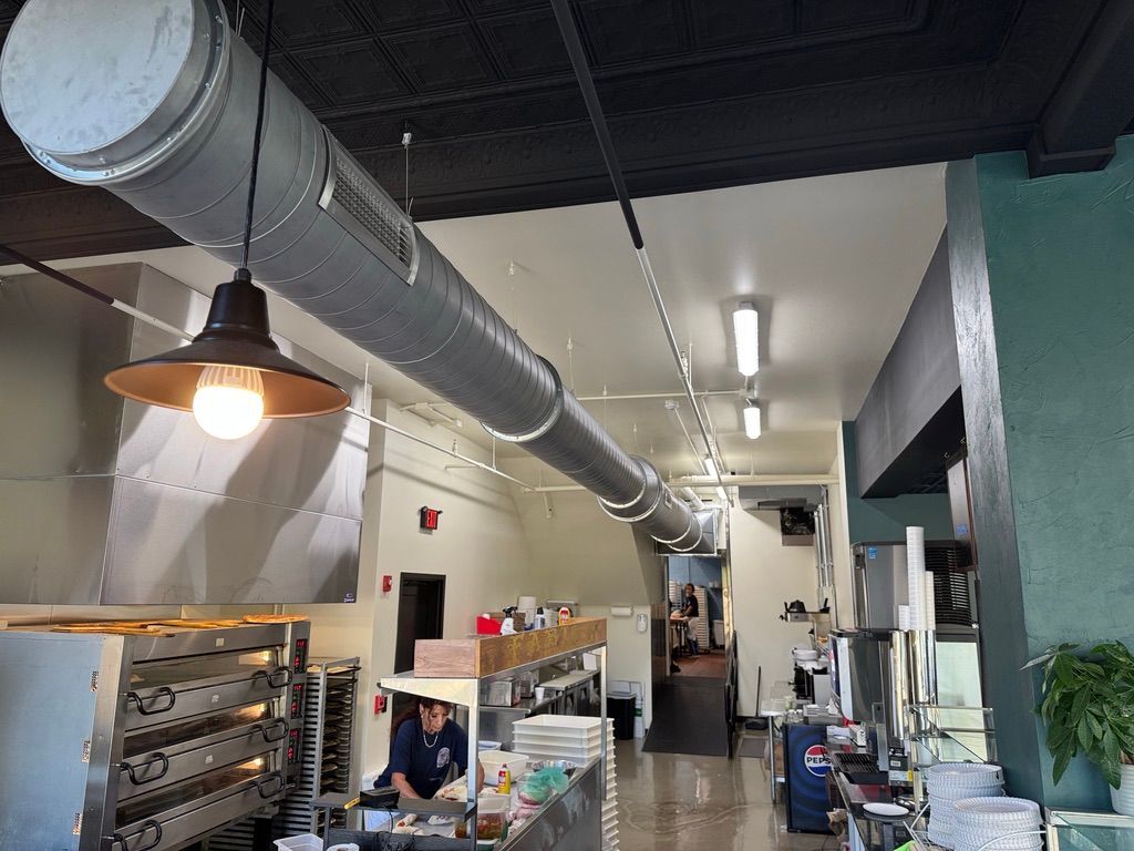 Bright industrial café interior with exposed ductwork, hanging lights, and a worker at a counter
