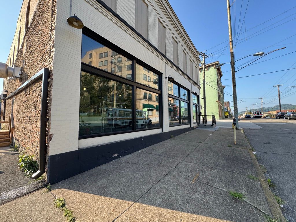 Storefront on a sunny street corner with large windows and brick siding, viewed from the sidewalk