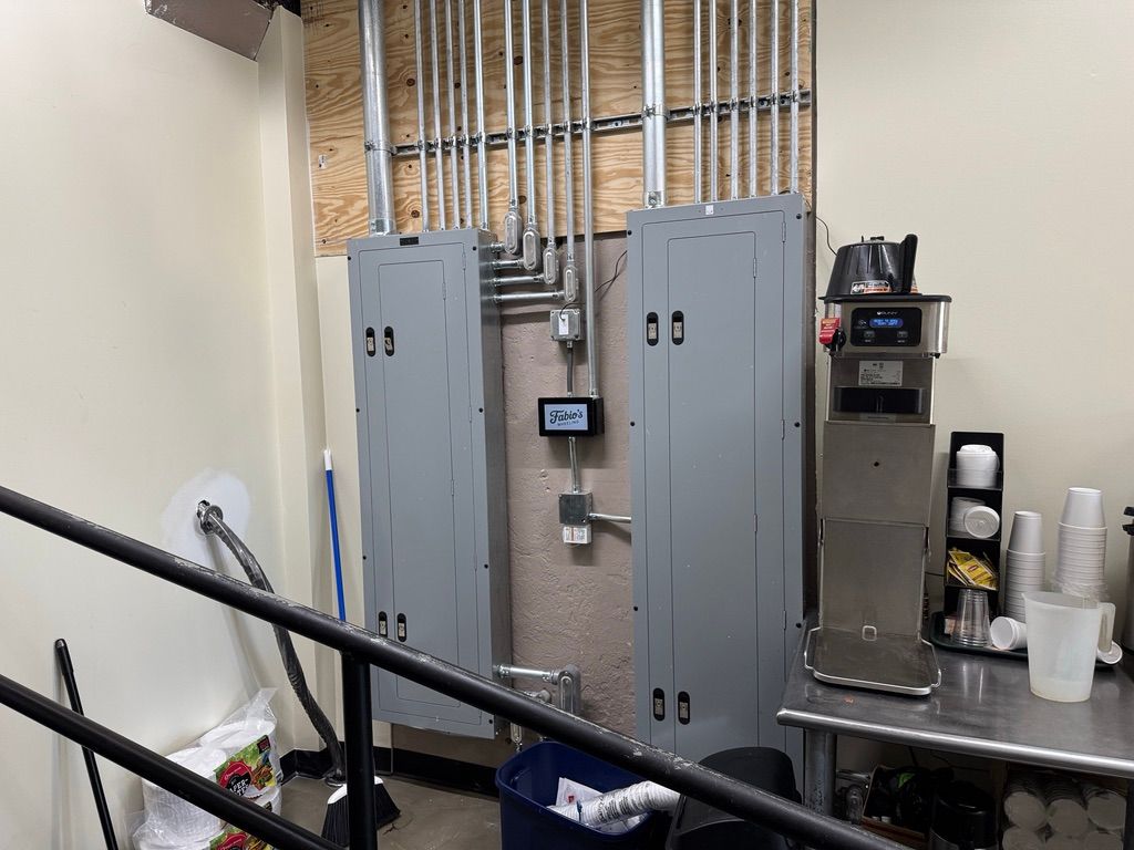 Utility room with electrical panels, exposed pipes, and a stainless-steel counter with cups and equipment.