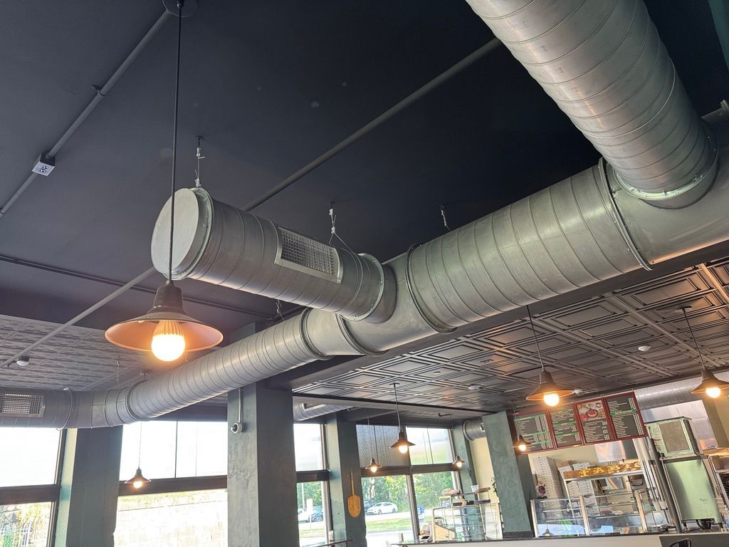 Industrial-style cafe ceiling with exposed ducts, hanging lights, and large windows below