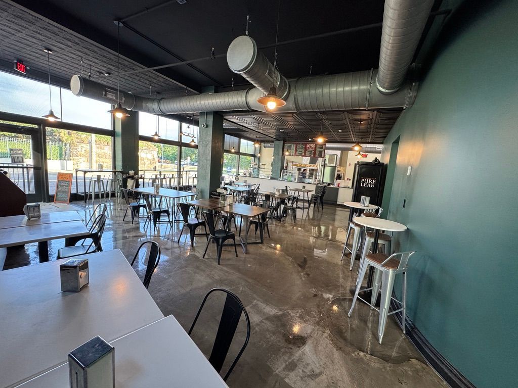 Modern café interior with empty tables, bar stools, industrial ceiling, and large windows
