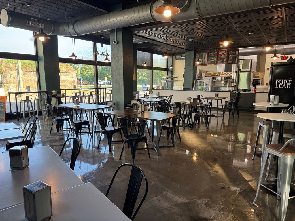 Empty modern café with black tables and chairs, polished floor, and large windows letting in daylight