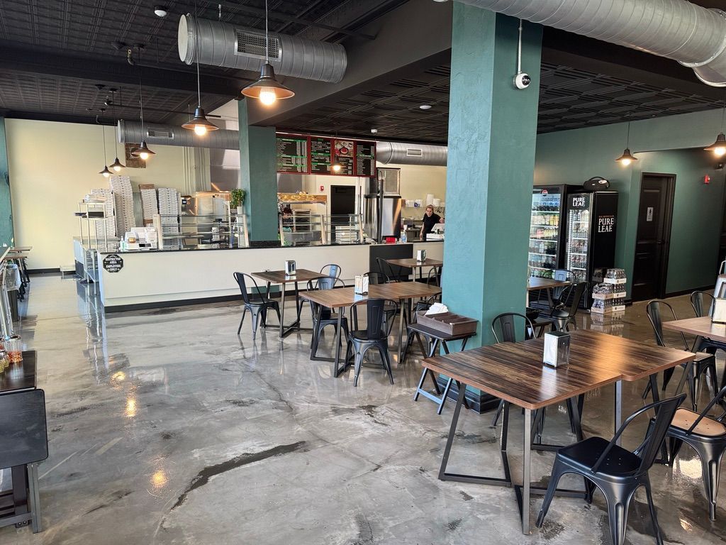 Empty modern café interior with wooden tables, black chairs, a long white counter, and exposed ceiling beams